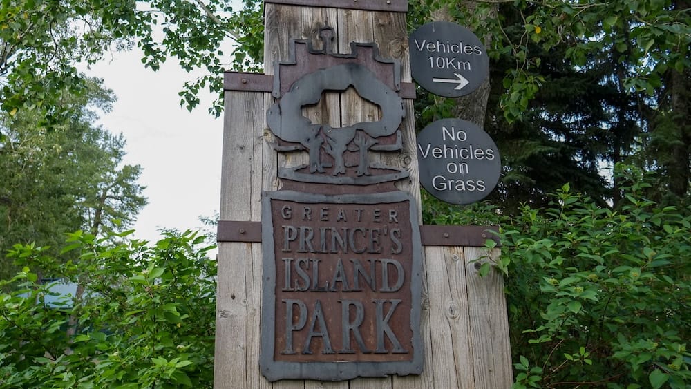 Greater Prince's Island Park entrance sign, Calgary, Alberta, Canada A wooden entrance sign reading "Greater Prince's Island Park" surrounded by trees in Calgary, Alberta, Canada, with a smaller sign noting no vehicles are permitted on the grass.