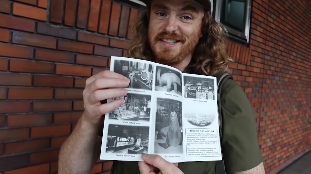 English brochure outside the Hakodate City Hokuyo Museum, Goryokaku, Hokkaido, Japan, held by Samuel Jeffery Samuel Jeffery holding an open English brochure outside the red brick exterior of the Hakodate City Hokuyo Museum in Goryokaku, Hakodate, Hokkaido, Japan, with photos of the taxidermy, simulator and fishing areas.