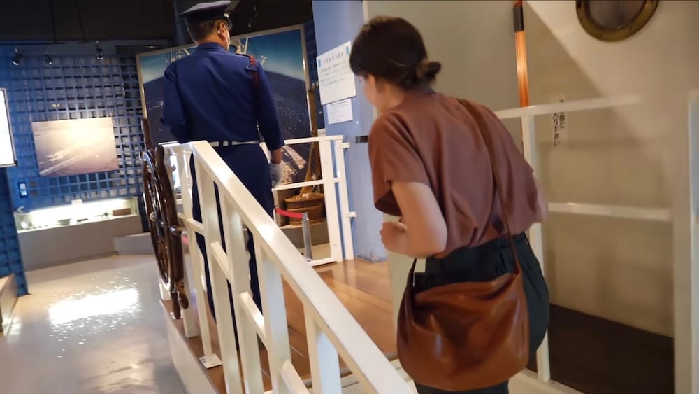 Audrey Bergner boards the fishing-boat simulator inside Hakodate City Hokuyo Museum in Hakodate, Hokkaido, Japan, while a Japanese attendant stands beside the simulated vessel.