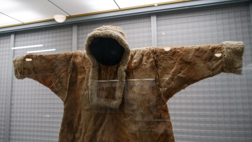 Fur hooded garment with wide outstretched sleeves and a fur-trimmed hood on display behind glass at the Hakodate City Museum of Northern Peoples in Hakodate, Hokkaido, Japan.