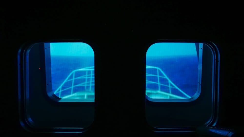 Blue-lit view through two simulator windows inside the Hakodate City Northern Pacific Fishery’s Document Museum in Hakodate, Hokkaido, Japan, showing the projected bow of a fishing boat during the rough-sea simulation.