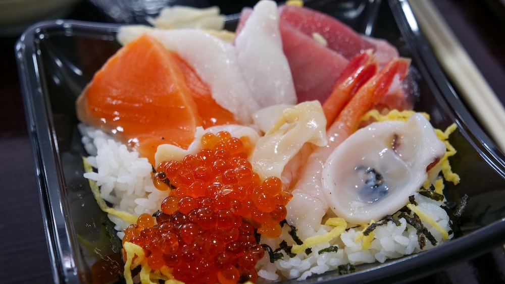 Close-up of a seafood rice bowl at Hakodate Morning Market in Hakodate, Hokkaido, Japan, topped with salmon roe, sashimi, squid and other fresh seafood over white rice.