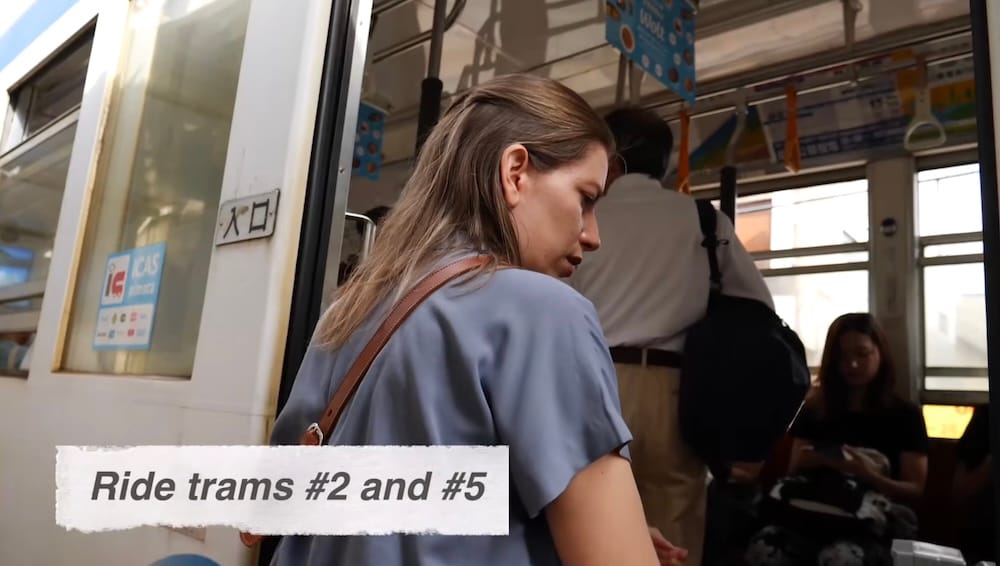 Audrey Bergner boards a Hakodate tram in Hokkaido, Japan, with passengers visible inside and an on-screen note referencing tram routes 2 and 5 used from the area where they stayed.