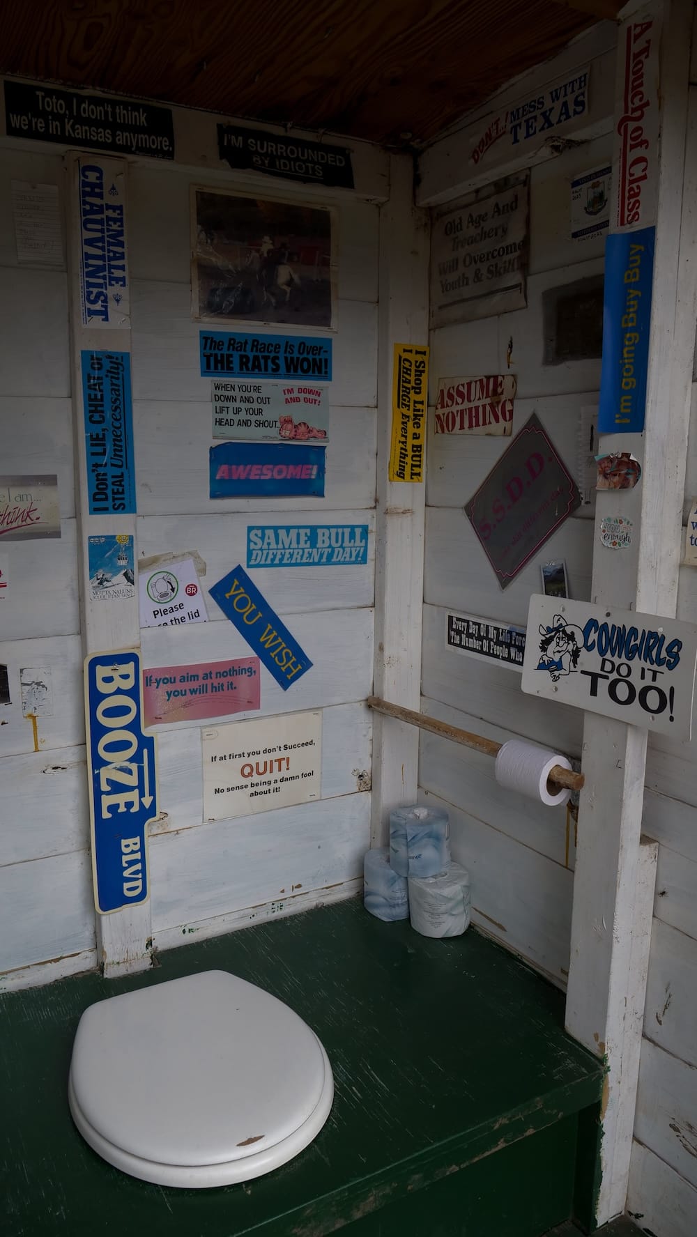 Letrina de Halfway Lodge en el Parque Nacional Banff, Alberta, Canadá, decorada con carteles y humor cowboy Interior rústico de la letrina de Halfway Lodge, Parque Nacional Banff, Alberta, Canadá, con inodoro sencillo, papel higiénico y paredes cubiertas de carteles, chistes y frases de cowboy.