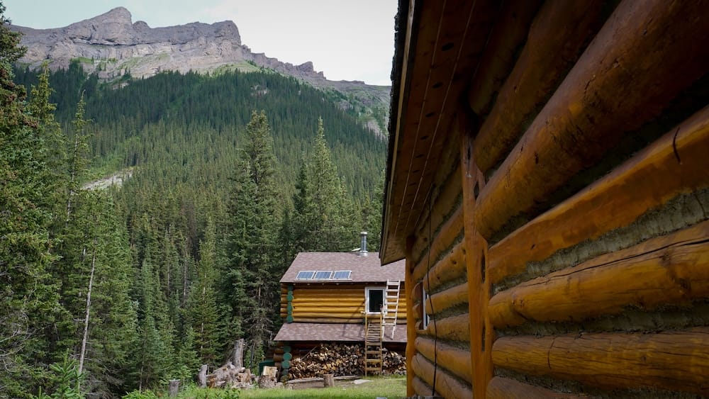 Cabañas de Halfway Lodge en el Parque Nacional Banff, Alberta, Canadá, bajo picos boscosos de las Montañas Rocosas Halfway Lodge en el Parque Nacional Banff, Alberta, Canadá, con paredes de troncos en primer plano, otra construcción rústica más abajo y empinadas laderas boscosas de las Montañas Rocosas detrás.