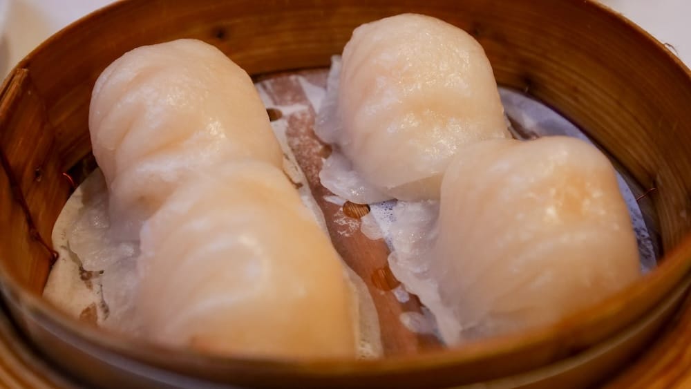 Har Gow Shrimp Dumplings at Silver Dragon Restaurant, Chinatown, Calgary, Alberta, Canada Four plump har gow shrimp dumplings with translucent wrappers in a bamboo steamer basket at Silver Dragon Restaurant in Chinatown, Calgary, Alberta, Canada.