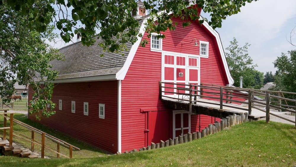 Heritage Park Calgary Alberta Canada Historic Red Barn Building at the Living History Attraction Large red historic barn-style building at Heritage Park in Calgary, Alberta, Canada, with white trim, a wooden access ramp, green grass and leafy trees surrounding the structure.