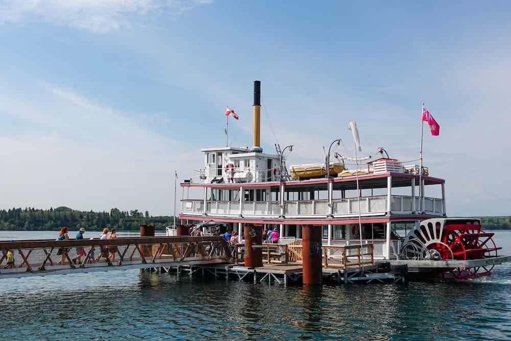 S.S. Moyie paddlewheeler docked on the Glenmore Reservoir at Heritage Park in Calgary, Alberta, Canada, with passengers walking along the pier beside the historic boat.