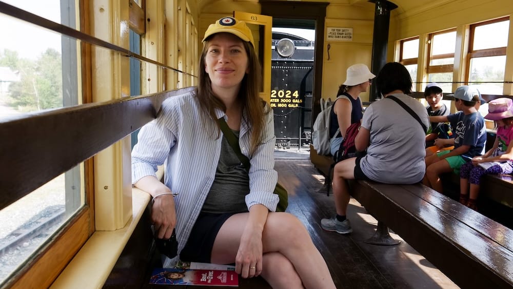 Audrey Bergner seated inside a vintage passenger car during the steam train ride at Heritage Park Historical Village in Calgary, Alberta, Canada, with other visitors riding behind her.