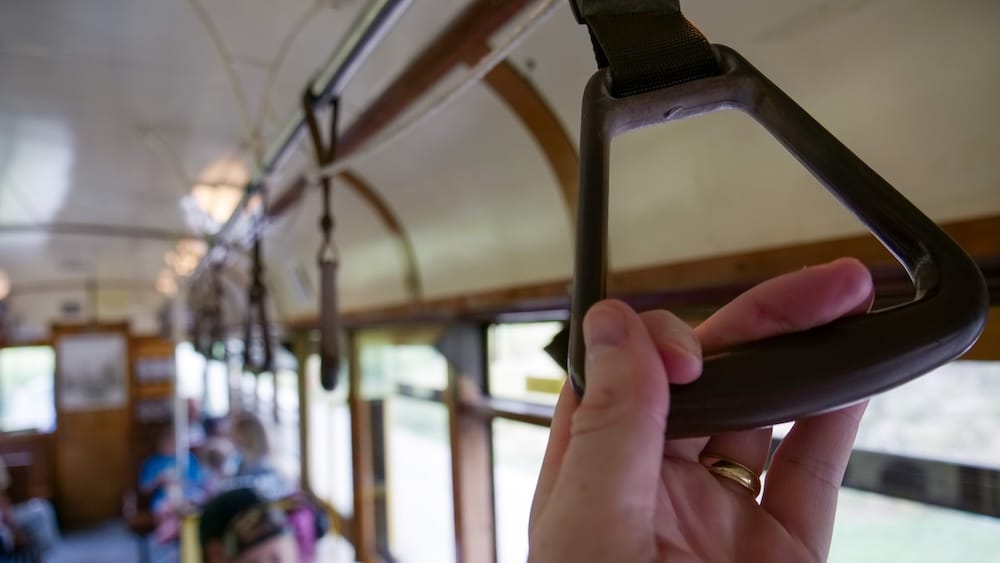 Interior hand strap aboard Edmonton’s High Level Bridge Streetcar in Alberta, Canada Close-up of a passenger’s hand holding a hanging strap inside Edmonton’s High Level Bridge Streetcar in Alberta, Canada, with the wooden heritage tram interior and seated riders softly blurred behind.