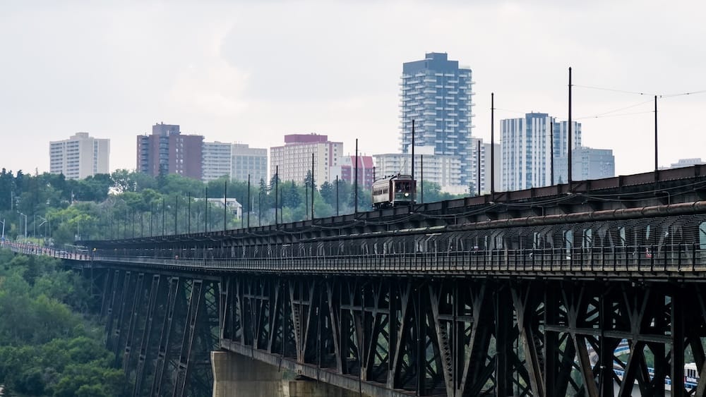 High Level Bridge Streetcar crossing the High Level Bridge in Edmonton, Alberta, Canada, with steel bridge trusses in the foreground and mid-rise downtown buildings rising beyond the North Saskatchewan River Valley.