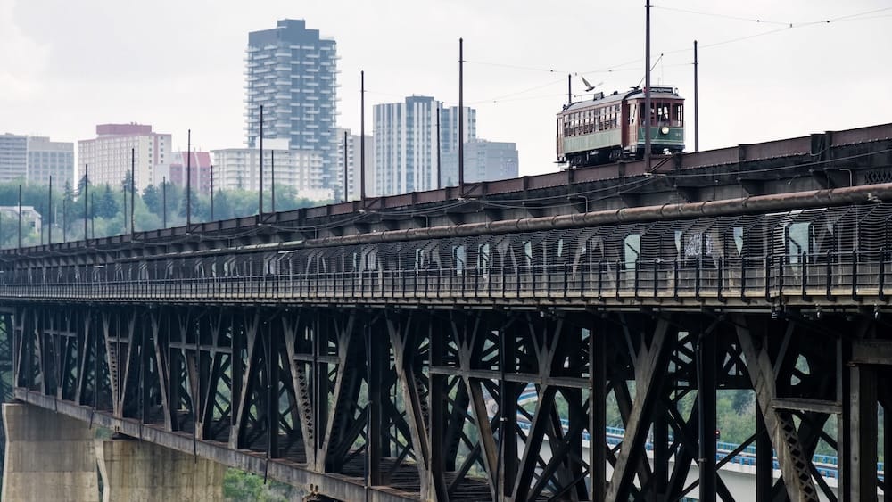 Historic High Level Bridge Streetcar crossing above Edmonton’s river valley in Alberta, Canada, with the bridge’s steel framework below and downtown apartment towers rising in the background.