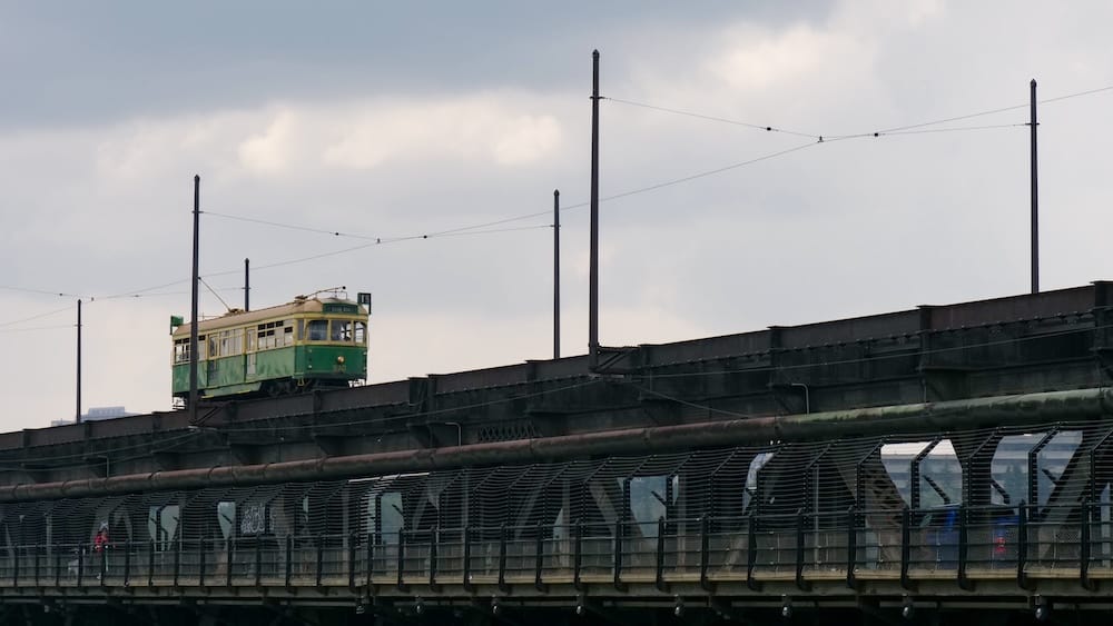 Vintage green High Level Bridge Streetcar crossing the bridge in Edmonton, Alberta, Canada, beneath overhead power lines with the pedestrian walkway visible below.