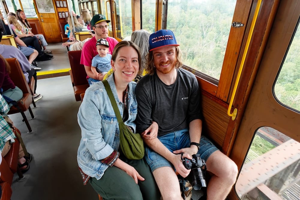 Samuel Jeffery and Audrey Bergner sit together inside Edmonton’s wood-panelled High Level Bridge Streetcar, with large windows overlooking the river valley in Edmonton, Alberta, Canada.