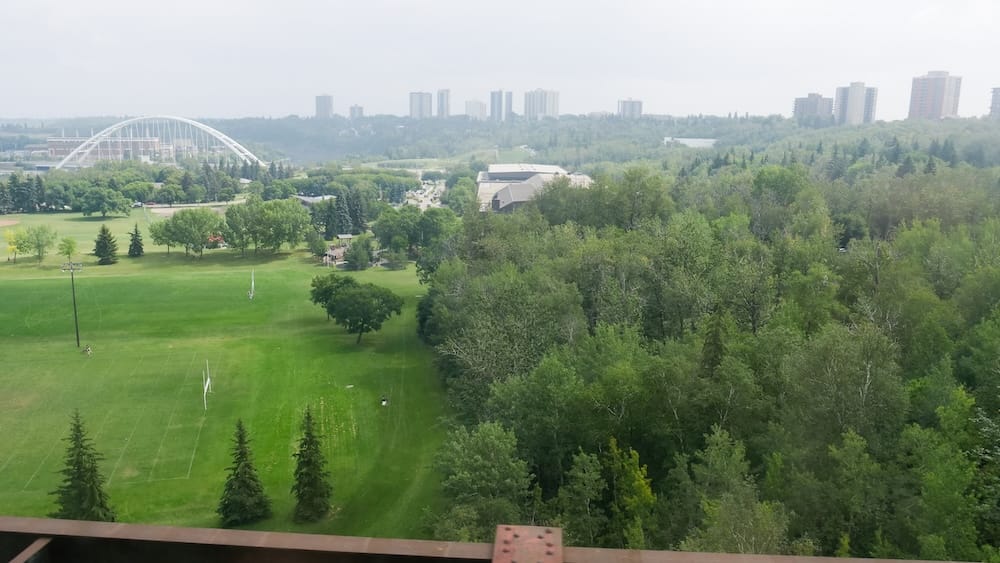 View from Edmonton’s High Level Bridge Streetcar in Alberta, Canada, looking across river-valley parkland toward Walterdale Bridge, dense trees and a distant line of downtown high-rises beyond the North Saskatchewan River.
