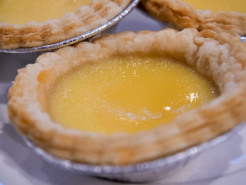 Close-up of a Hong Kong-style egg tart with a smooth, glossy yellow custard and flaky pastry shell at Chinese Cultural Centre Cuisine in Calgary, Alberta, Canada.