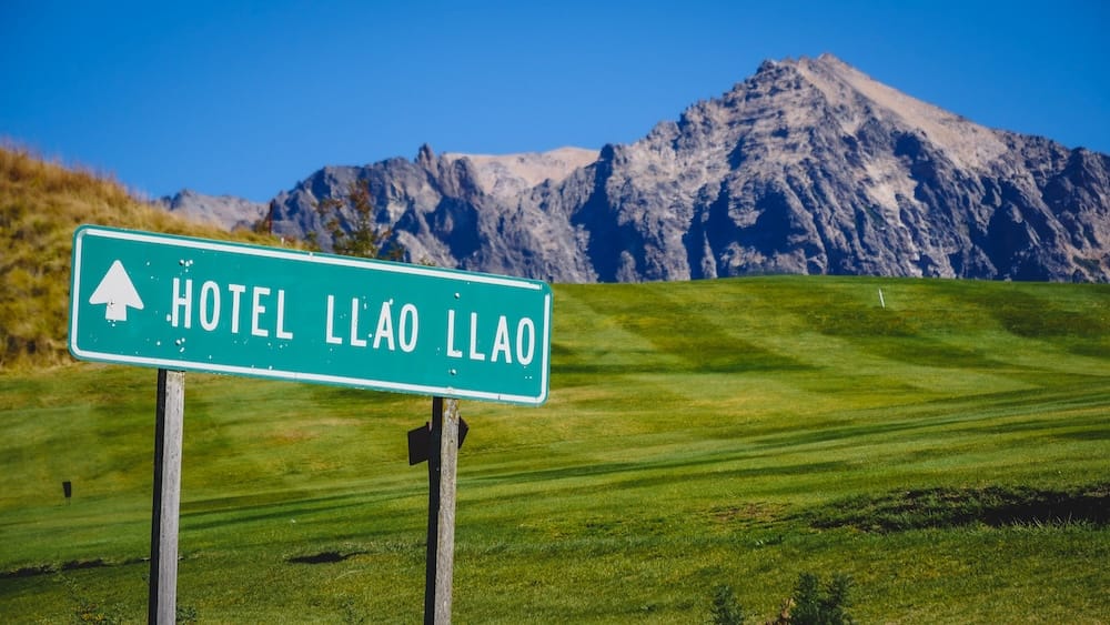 Hotel Llao Llao directional sign, golf course, Andes mountains, Bariloche, Río Negro, Argentine Patagonia A green "Hotel Llao Llao" directional sign with an arrow, staked in a grassy fairway with rugged Andes peaks rising behind it, near Bariloche, Río Negro, in Argentine Patagonia.
