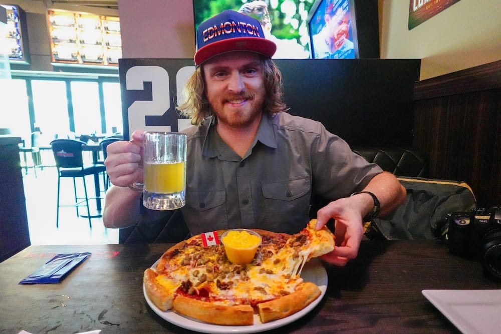 Ice House Sports Bar, Meaty Pizza and Craft Beer, ICE District, Edmonton, Alberta, Canada Samuel Jeffery wearing a new Edmonton Oilers hat, holding a craft beer beside a meat-topped pizza and cheddar dip at Ice House sports bar near Rogers Place, Edmonton, Alberta, Canada.