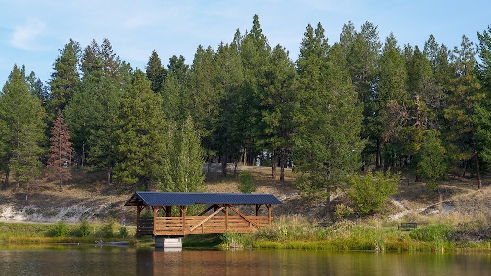 Idlewild Park in Cranbrook, British Columbia, showing calm water, tall pine trees, and open green space that highlights why this peaceful local park was one of the most tranquil and relaxing places we experienced while exploring the city.
