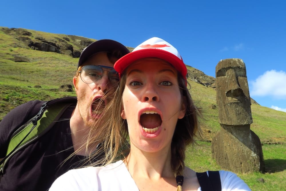 Isla de Pascua, Chile con Samuel Jeffery y Audrey Bergner junto a un moai, mostrando una experiencia real en uno de los destinos más remotos del mundo y exploración de sitios arqueológicos únicos.