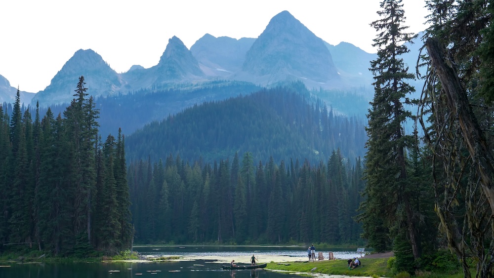 Canoeing on the alpine lake at Island Lake Lodge in Fernie, British Columbia, with visitors paddling across calm water framed by evergreen forest and dramatic mountain peaks, highlighting one of the most peaceful summer activities available at the lodge.
