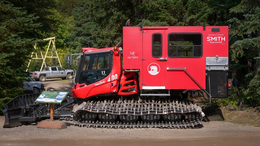 Snowcat vehicle used for winter access and cat-skiing operations at Island Lake Lodge in Fernie, British Columbia, shown parked near the trailhead and forest edge, highlighting the specialized tracked transport essential for deep-snow skiing adventures.
