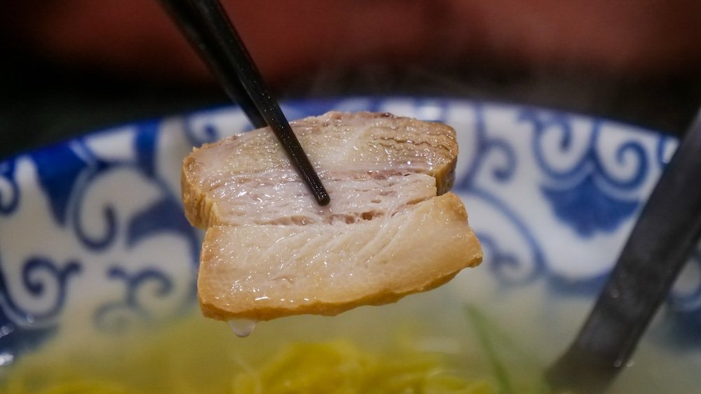 Japanese ramen pork held by chopsticks dripping broth macro shot 