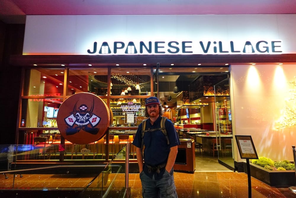 Samuel Jeffery Outside Japanese Village in West Edmonton Mall, Edmonton, Alberta, Canada Samuel Jeffery stands outside Japanese Village in West Edmonton Mall, Edmonton, Alberta, Canada, beneath the illuminated restaurant sign and beside its decorative entrance display.