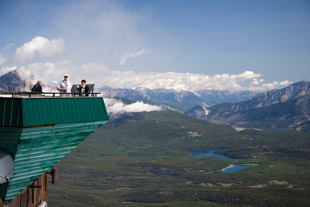 Jasper SkyTram upper station in Jasper National Park, Alberta, Canada, with visitors on the observation deck overlooking forested valleys, mountain ridges and small alpine lakes.