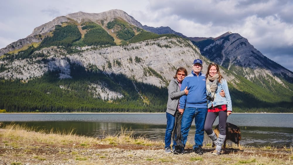Audrey Bergner with Daniel and Maria Bergner and Togo at a mountain lake in Kananaskis Country, Alberta, Canada Audrey Bergner stands with Daniel Bergner, Maria Bergner and Togo beside a mountain lake in Kananaskis Country, Alberta, Canada, with forested slopes and broad rocky peaks behind them.