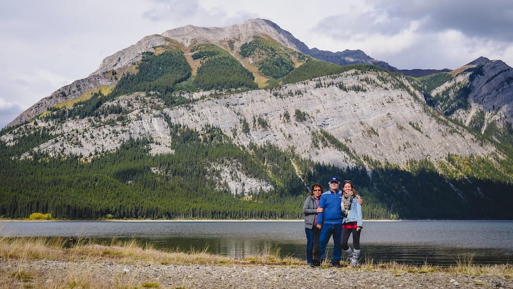Kananaskis Country, Alberta, Canada with Audrey Bergner, Daniel Bergner and Maria Bergner beside a mountain lake Audrey Bergner standing with her parents Daniel Bergner and Maria Bergner beside a mountain lake in Kananaskis Country, Alberta, Canada, with forested slopes and rocky peaks behind them.