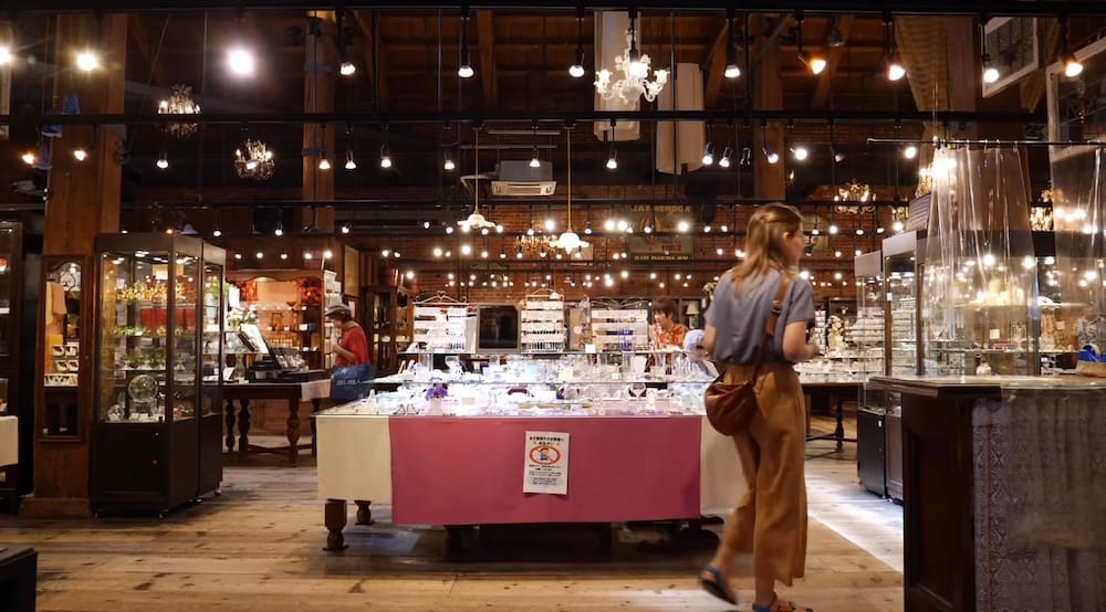 Audrey Bergner walks through an indoor shop at the Kanemori Red Brick Warehouses in Hakodate, Hokkaido, Japan, surrounded by display cases, wooden beams, chandeliers and souvenir merchandise.