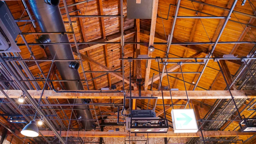 Historic Timber Roof Structure and Exposed Wooden Ceiling Inside Kanemori Red Brick Warehouses, Hakodate, Japan Interior ceiling of the Kanemori Red Brick Warehouses in Hakodate, Hokkaido, Japan, showing exposed wooden rafters, heavy timber beams, metal support frames, black ventilation ducts and suspended industrial lighting.
