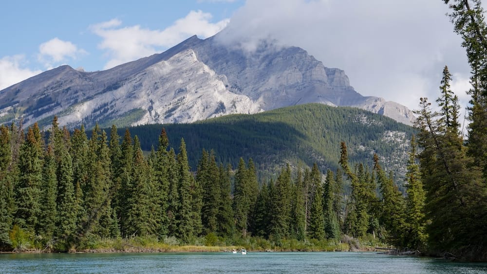 Dos kayakistas a lo lejos remando por el río Bow cerca de Banff, Alberta, Canadá, enmarcados por la densa vegetación de la orilla y el bosque en la ribera opuesta.