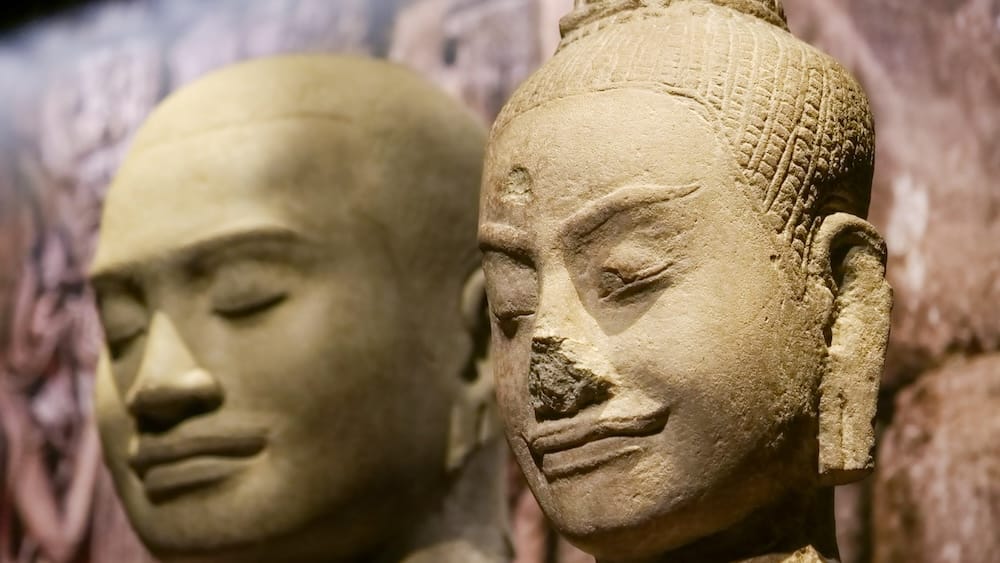 Réplicas de cabezas de piedra jemer, antigua exhibición de Angkor Wat, Royal Alberta Museum, Edmonton, Alberta, Canadá Dos serenas réplicas de cabezas de piedra talladas con los ojos cerrados y tocados tradicionales jemer se exhiben muy juntas, parte de una antigua exhibición especial de Angkor Wat que alguna vez se mostró en el Royal Alberta Museum en Edmonton, Alberta, Canadá.