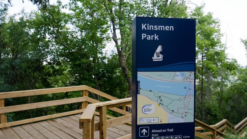 Mapa de senderos y acceso por escaleras en Kinsmen Park, River Valley de Edmonton, Canadá Mapa de senderos y cartel de orientación de Kinsmen Park junto a escaleras de madera en Edmonton, Alberta, Canadá, rodeado por árboles frondosos del River Valley.