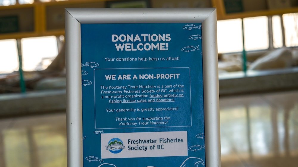 Donation sign inside the Kootenay Trout Hatchery near Cranbrook, BC, explaining that the facility is a non-profit operated by the Freshwater Fisheries Society of BC and supported through fishing licence revenue and visitor donations.