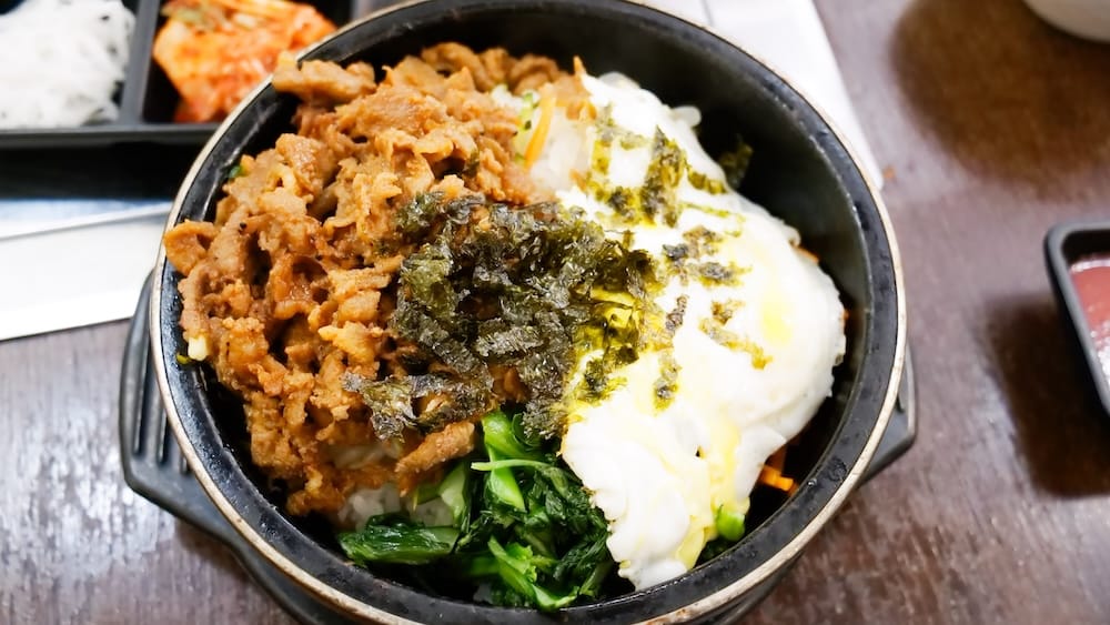 Dolsot bibimbap, a Korean dinner in Calgary, Alberta, Canada A sizzling stone-bowl dolsot bibimbap topped with pork, egg, seaweed, and greens, served with banchan side dishes at a Korean restaurant in Calgary, Alberta, Canada.