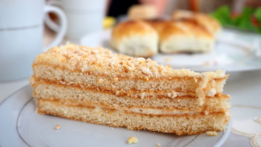 Close-up of a slice of layered Kyrgyz honey cake served in Karakol, with thin sponge layers, creamy filling and a crumb topping, photographed after a family meal during our food travels in Kyrgyzstan.
