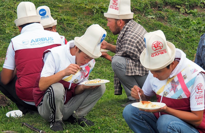 Kyrgyz men squatting down to enjoy a plate of Plov during the Games