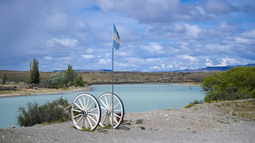 La Leona roadside stop on Route 40 between El Calafate and El Chaltén, with lake views and an Argentine flag, marking the iconic halfway break for travelers riding the Patagonia bus route.
