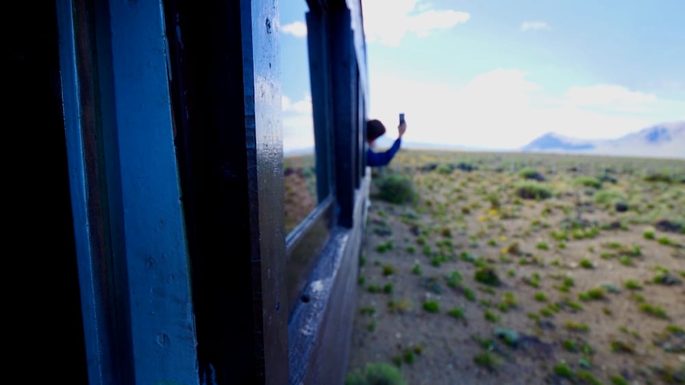 Passenger Photographing the Patagonian Steppe from La Trochita in El Maitén, Chubut, Argentina A passenger leans from a carriage window to photograph the open Patagonian steppe during a ride on La Trochita near El Maitén, Chubut, Patagonia, Argentina.