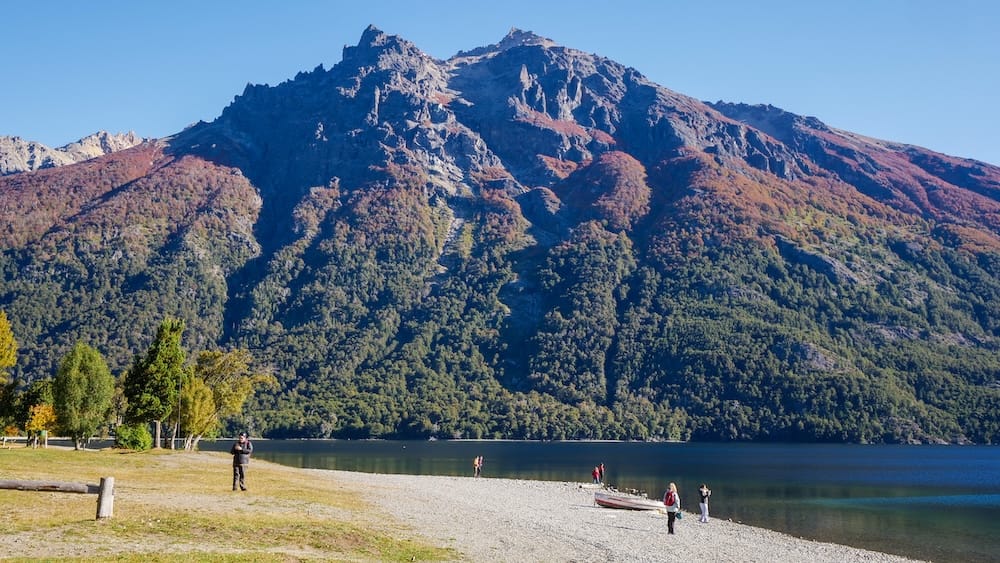 Lago Gutiérrez in Bariloche with clear autumn water and steep mountain peaks in Patagonia Argentina Lago Gutiérrez in Bariloche Río Negro Argentina during autumn, showing clear blue water and steep Andean mountain peaks with forested slopes transitioning to fall colors under calm-looking Patagonian conditions.