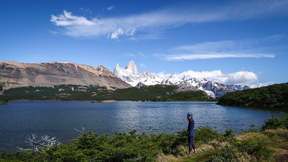 Laguna Capri in El Chaltén, Patagonia, with turquoise lake and Mount Fitz Roy towering behind, as Audrey Bergner stands at the shoreline presenting the classic viewpoint, capturing Argentina’s iconic hiking capital scenery.