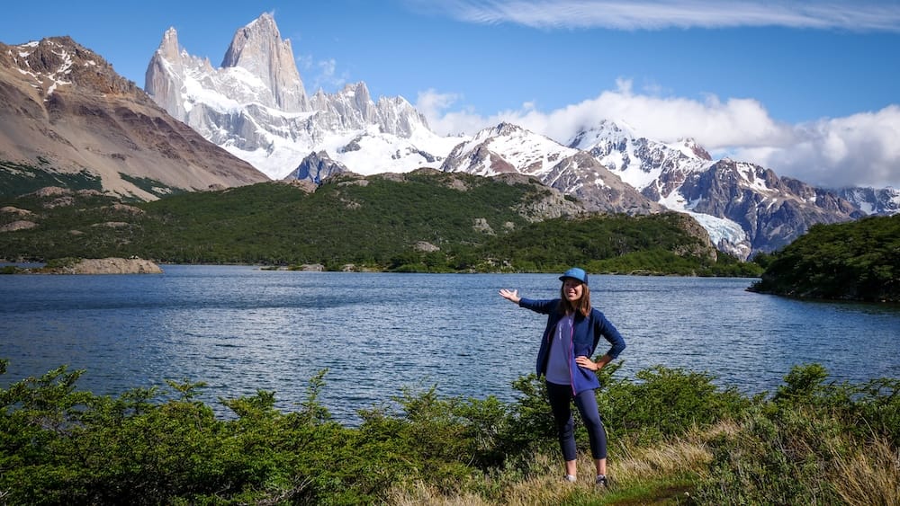 Laguna Capri and Mount Fitz Roy Near El Chaltén, Patagonia, Argentina, with Audrey Bergner Audrey Bergner stands beside Laguna Capri near El Chaltén, Santa Cruz, Patagonia, Argentina, presenting the snow-covered Mount Fitz Roy skyline above blue water, green forest and glacier-cut mountains.