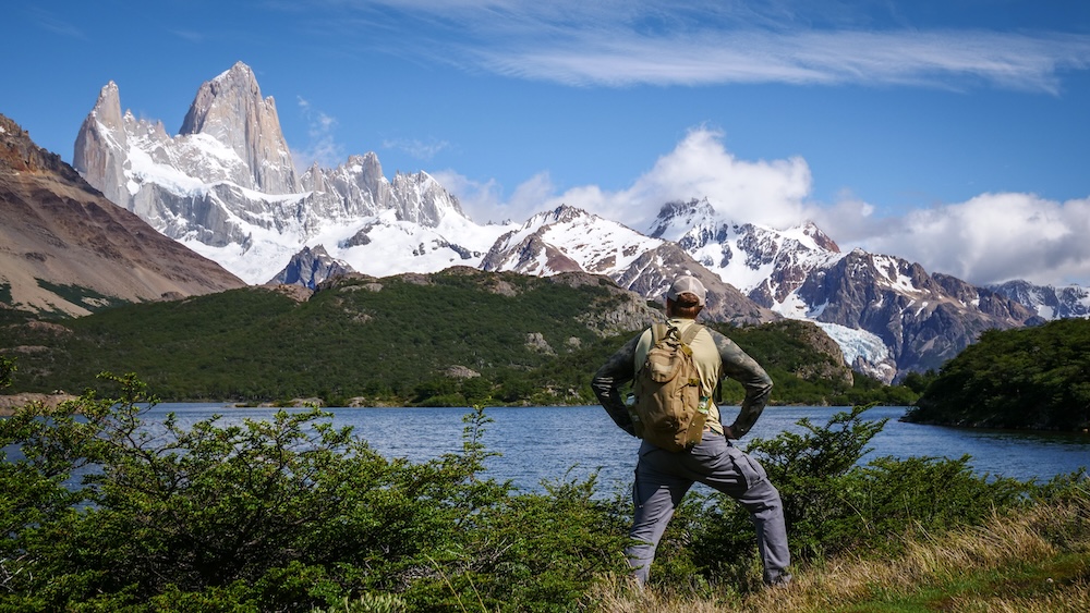 Laguna Capri, El Chaltén, Patagonia, Argentina—Nomadic Samuel stands at the iconic lakeshore lookout with Fitz Roy towering above, a classic pause on the Laguna de los Tres hike before the final steep push.
