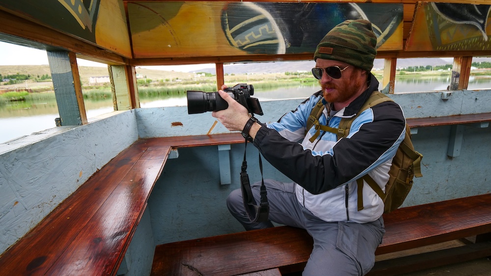 Laguna Nimez bird reserve in El Calafate day trip Laguna Nimez in El Calafate, Patagonia, Argentina, with Nomadic Samuel photographing wetland birdlife from a wooden viewing shelter — a calm nature reserve and easy day trip option from El Chaltén when mountain weather turns moody