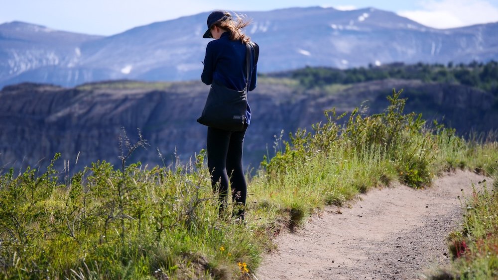 Laguna Torre trailhead, El Chaltén, Patagonia: Audrey Bergner pauses along the path to take in sweeping mountain scenery, with grassy edges, a winding dirt trail, and layered Patagonian ridgelines emphasizing the calm before the longer hike ahead.
