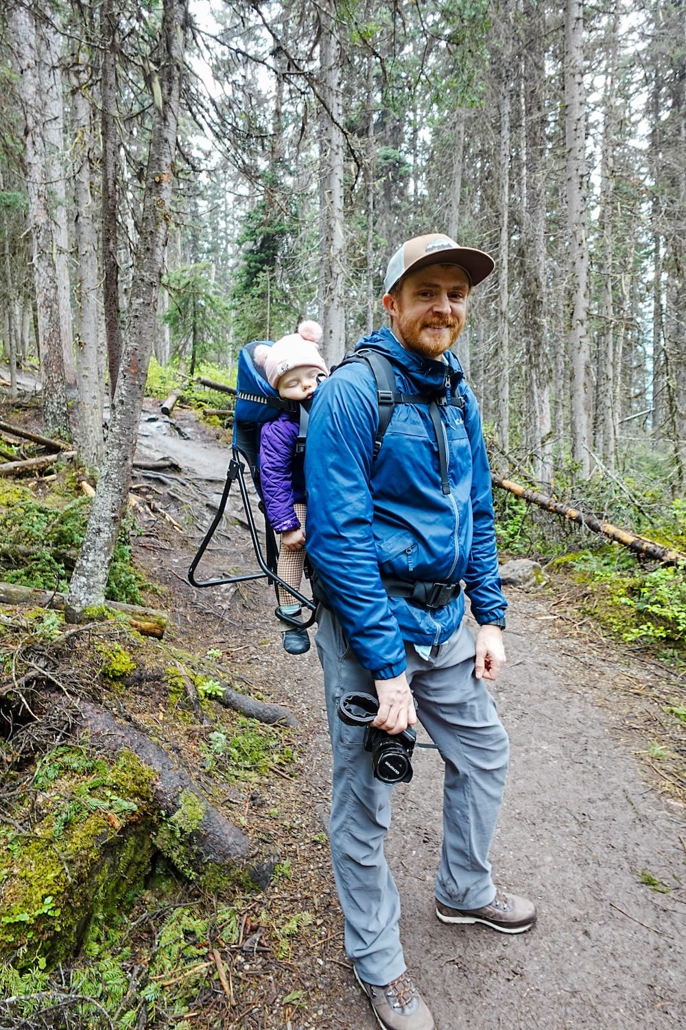 Samuel Jeffery camina por un sendero boscoso cerca de Lake Louise, Alberta, Canadá, cargando a Aurelia Jeffery profundamente dormida en una mochila portabebé mientras lleva su cámara.