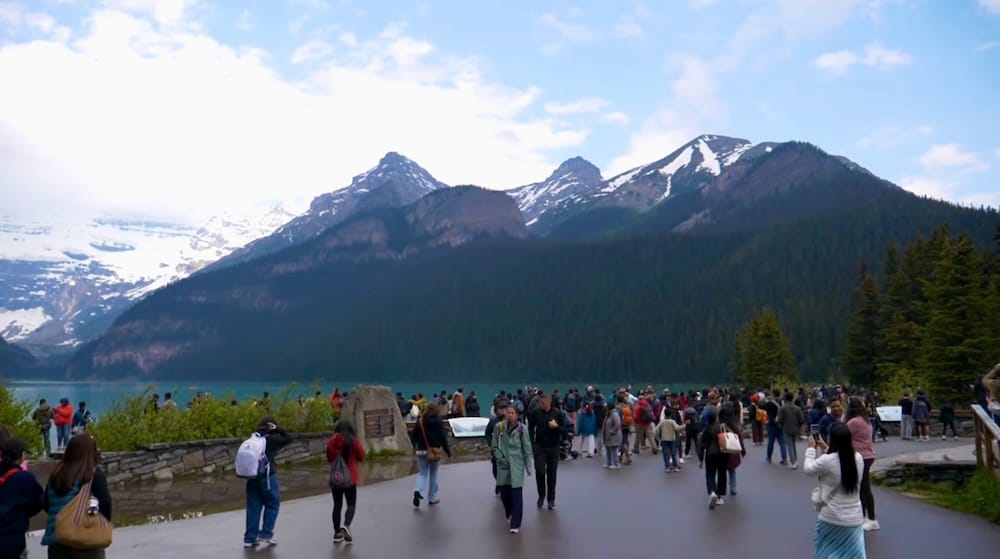 Busy Lake Louise shoreline in Banff National Park Alberta Canada with crowds mountain views and turquoise water Large crowds gather along the Lake Louise shoreline in Banff National Park, Alberta, Canada, with turquoise water, forested mountains and lingering snow visible behind the busy viewing area.